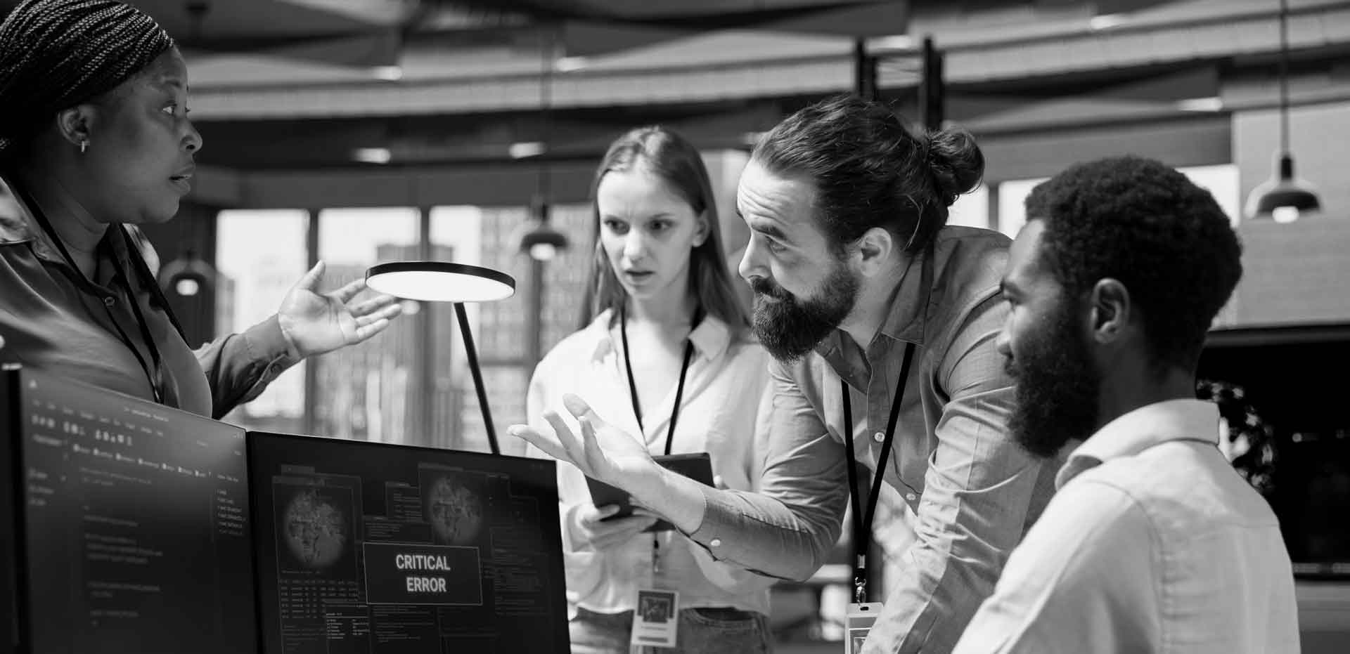 A development team gathered around monitors, one of which reads CRITICAL ERROR